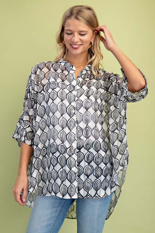 Loose fit sheer lurex button down top with hi-low hem, modeled by a woman against a green background.