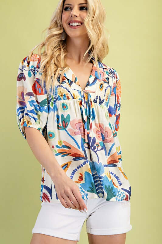 Model wearing the Summer Nights Collared Blouse with colorful floral print and tie strings in front, paired with white shorts.